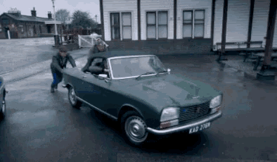 a man pushing a green car with a license plate that says kad 2078
