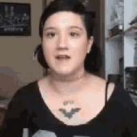 a woman with a bat tattoo on her chest is wearing a black shirt and necklace .