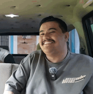 a man with a mustache wearing a gray shirt that says nasuda