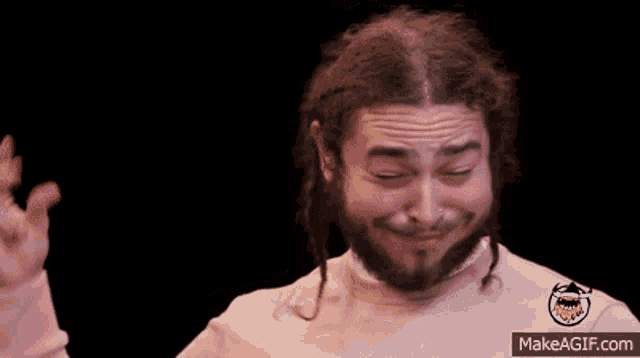 a man with dreadlocks and a beard is wearing a pink sweater with a yellow smiley face on it