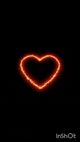 a heart made of fire is glowing in the dark on a black background .
