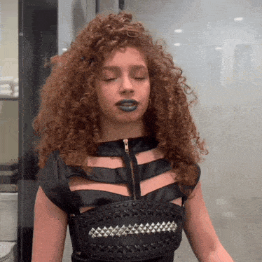 a woman with curly hair wears a black top with studs on it