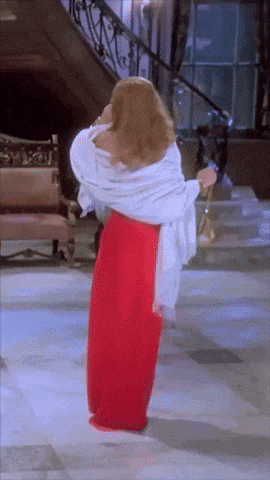 a woman in a red skirt and white shawl is dancing in a room