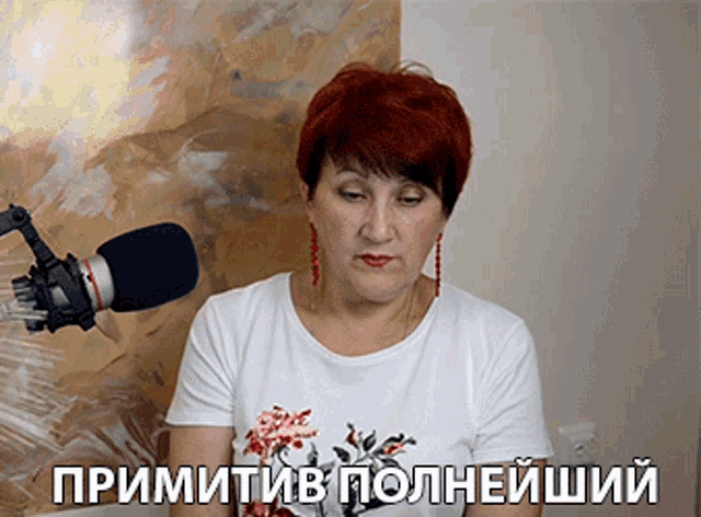 a woman in a white shirt stands in front of a microphone with the words primitiv on the bottom right
