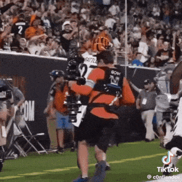a man is carrying a camera on his back while a football player runs towards him .