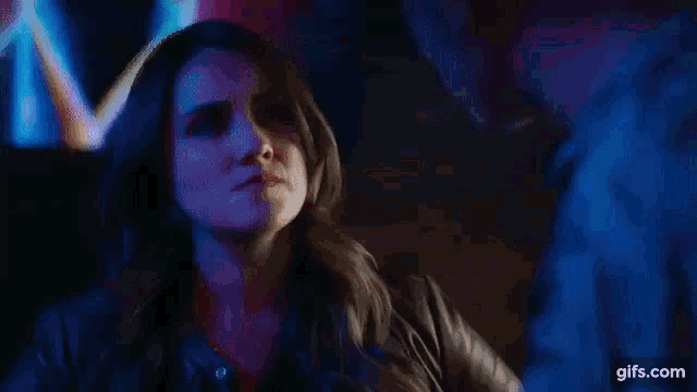 a woman is sitting in a dark room with a man behind her .