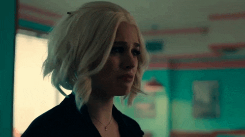a woman with blonde hair and a necklace is standing in a dark room .