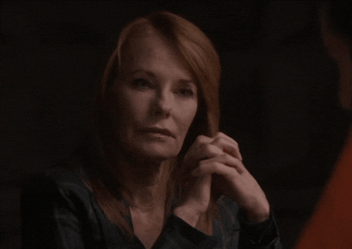 a woman with red hair is sitting with her hands folded in front of her face