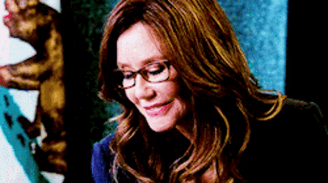 a woman wearing glasses is smiling and looking down .