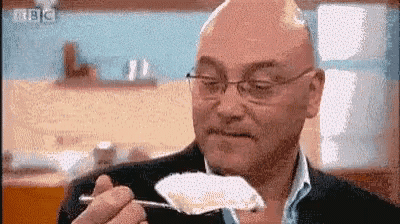 a bald man wearing glasses is eating a piece of food with a spoon .