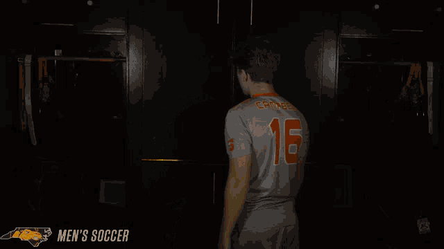 a man wearing a jersey with the number 16 on it prays in a dark room