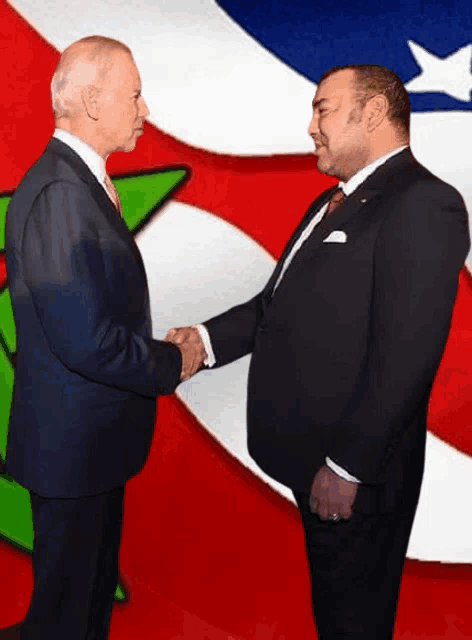 a man in a suit shakes hands with another man in front of an american flag