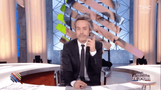 a man in a suit and tie is sitting at a desk in front of a screen that says tmc