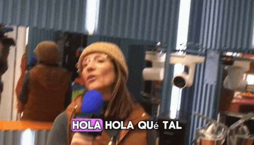 a woman holding a microphone with the words hola hola que tal written above her