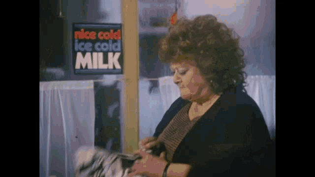 a woman sitting in front of a sign that says ice cold milk