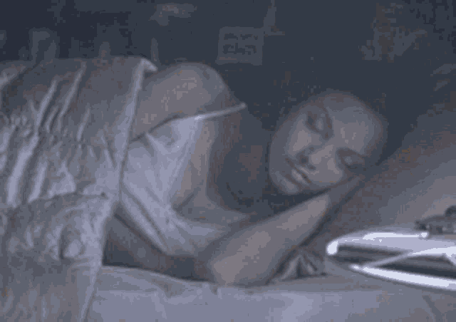 a woman in a white tank top is sleeping in a bed .