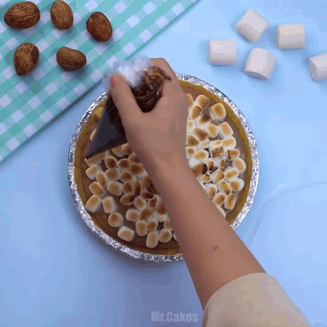 a person is making a pie with marshmallows and nuts and the word mr.cakes is on the bottom