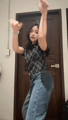 a young woman in a plaid shirt and jeans is dancing in front of a wooden door .