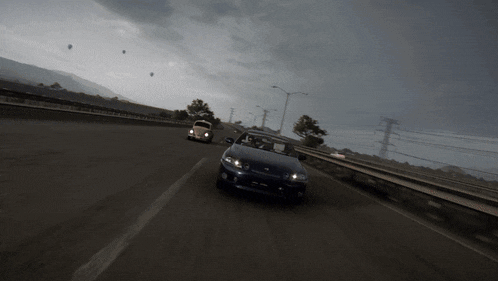 two cars are driving down a highway with a cloudy sky