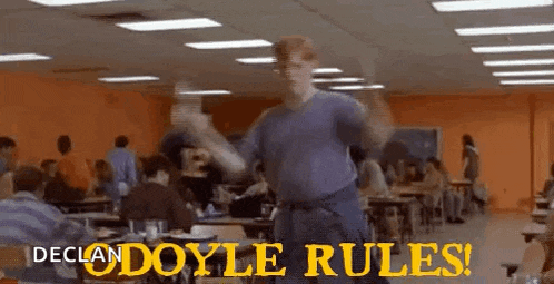 a man is dancing in a cafeteria with the words `` declan doyle rules '' written on the bottom .