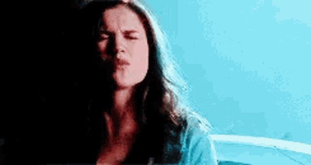 a woman with long hair is making a funny face in a dark room with a blue sky in the background .