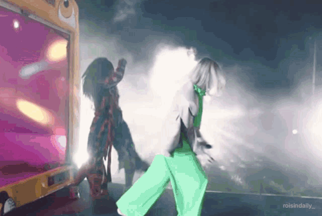 two women in green pants are dancing on a stage in front of a yellow truck that says raisindaily