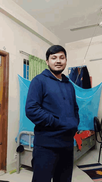 a man in a blue hoodie stands in a bedroom