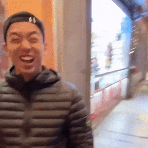 a man wearing a hat and a black jacket is laughing while walking down a street .
