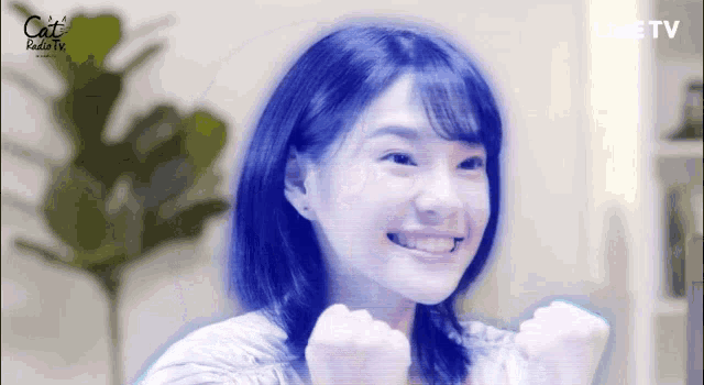 a woman with blue hair is smiling with her fist in the air