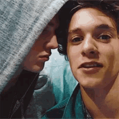 two young men are standing next to each other and one of them is wearing a hooded jacket .
