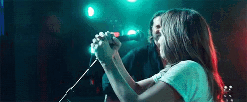 a woman is singing into a microphone on stage while a man plays a guitar .