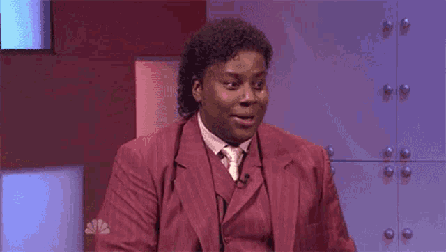 a man in a red suit and tie is making a surprised face while sitting on a stage .
