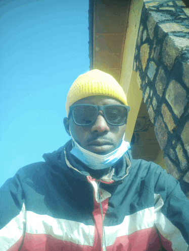 a man wearing a yellow beanie and sunglasses takes a selfie