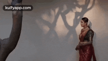 a woman in a red saree is standing in front of a statue .