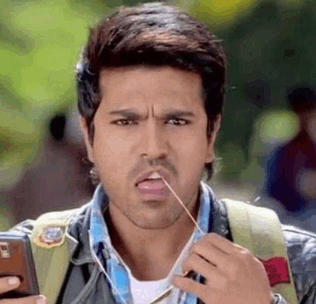 a man is holding a cell phone in his hand and sticking a toothpick in his mouth .