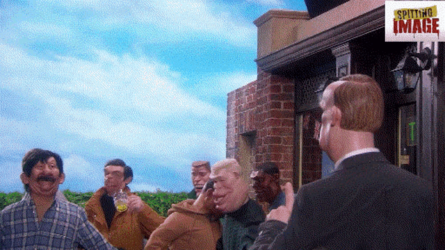 a group of men standing outside of a building with spitting image written on the bottom right