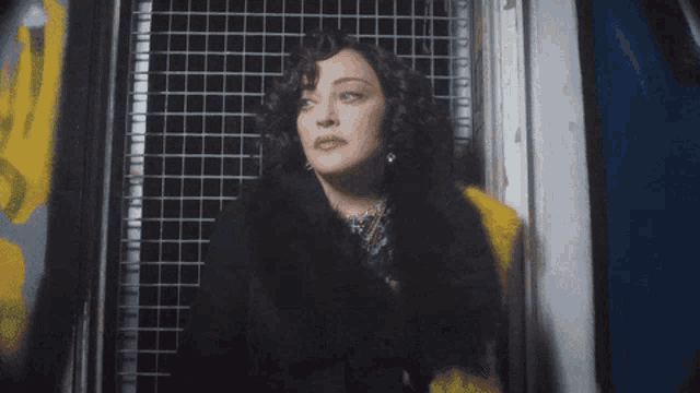 a woman in a fur coat stands in front of a window