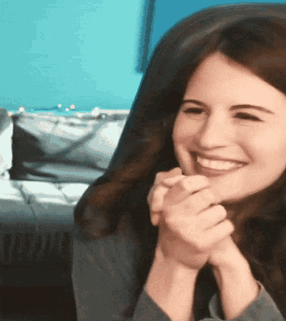 a woman sitting in a chair smiling with her hands folded