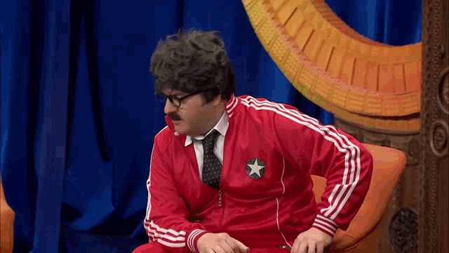 a man with glasses and a mustache is wearing a red jacket and tie .