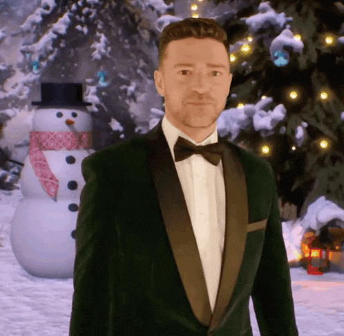 a man in a tuxedo stands in front of a snowman and a christmas tree