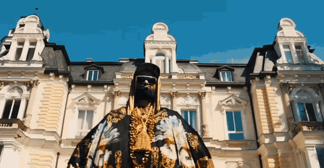 a man in a black and gold outfit stands in front of a building