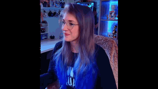 a woman with purple hair and glasses is sitting in front of a desk .