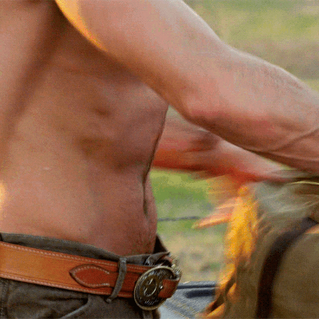 a man without a shirt is wearing a brown belt with a buckle that says " cowboy "