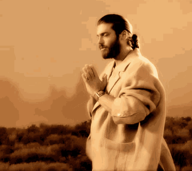 a man with a beard is praying with his hands folded in front of a field