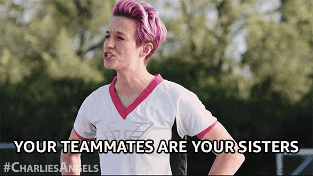 a woman with pink hair is wearing a white shirt that says " your teammates are your sisters "