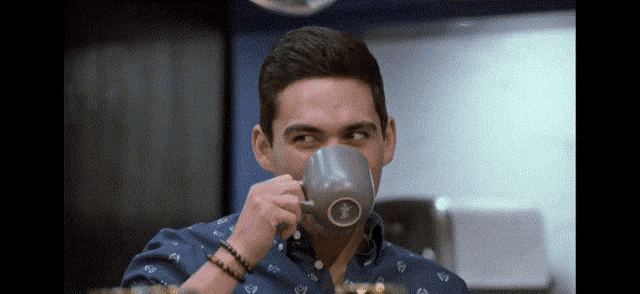a man in a blue shirt is drinking from a coffee mug with a bird on it