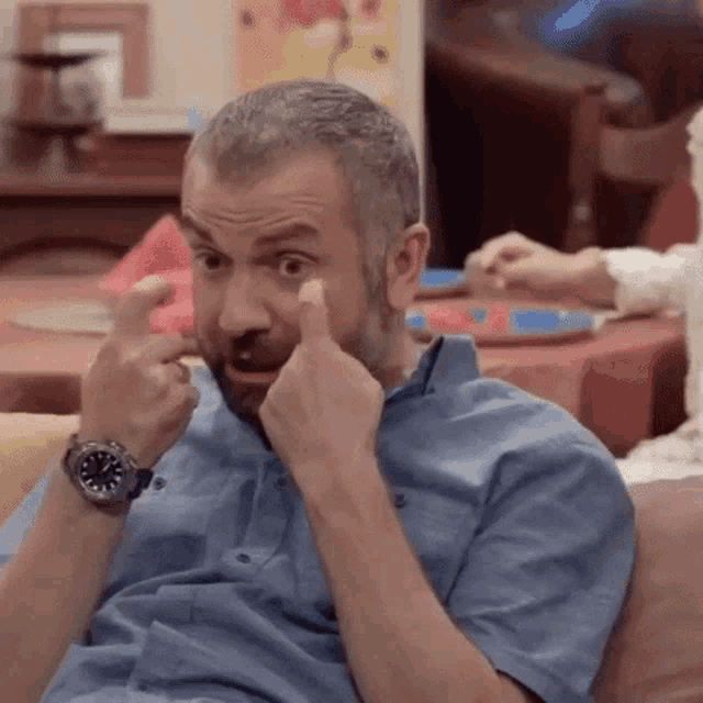 a man with a beard is sitting on a couch making a funny face with his hands .