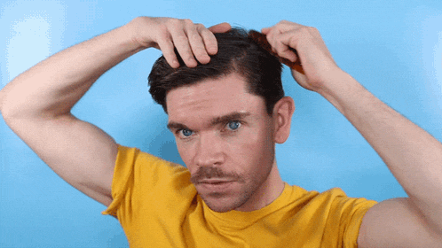 a man in a yellow shirt is brushing his hair with a comb