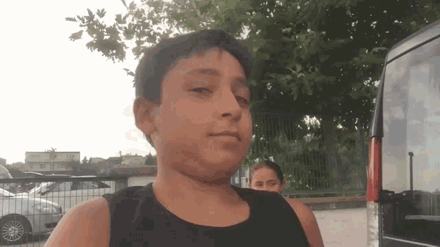 a boy in a black tank top is standing in front of a fence