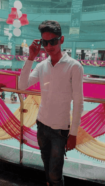 a young man wearing sunglasses and a white shirt stands in front of a pink wall